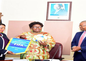 The Speaker (C) receives a ball and FIFA pennant from Samoura as FUFA President Magogo looks on