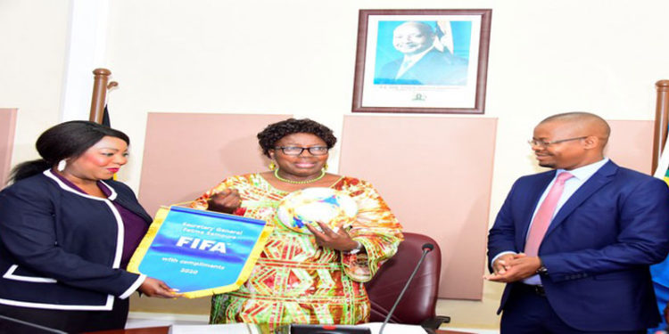 The Speaker (C) receives a ball and FIFA pennant from Samoura as FUFA President Magogo looks on