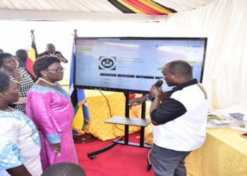 The Speaker(C) accompnaied by the Leader of the Opposition and Government Chief Whip listen to the Director, ICT Fred Bbale explain how the App works