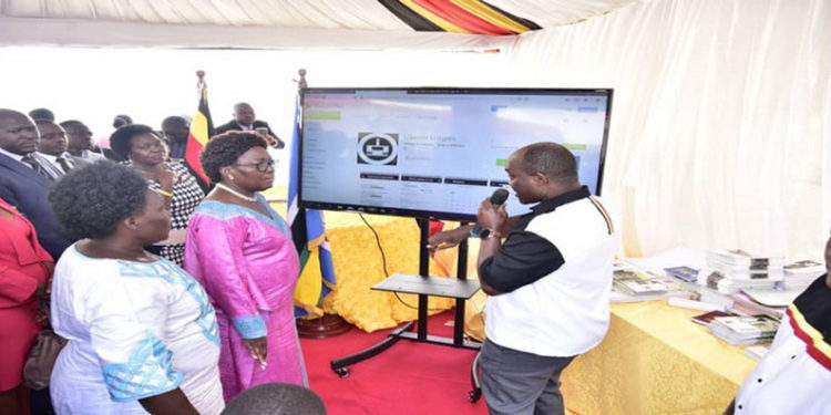 The Speaker(C) accompnaied by the Leader of the Opposition and Government Chief Whip listen to the Director, ICT Fred Bbale explain how the App works