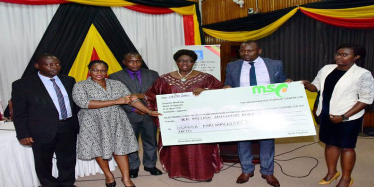 Speaker Kadaga (C) hands over a dummy cheque to the UPPA. On her left is Hon Kasolo Kyeyune with Hon Bahati(L) looks on
