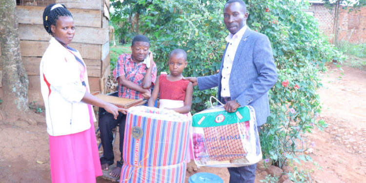 Dorothy Nakiryowa receiving donated items; Bed sheet and a blanket from Gideon Kabenge who is currently taking care of his brother Ssebaduka.