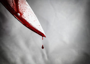 close-up of man holding knife smeared with blood and still dripping.