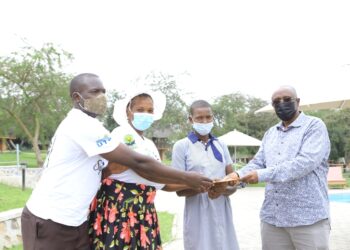 Brig Bakahumura hands over the envelope to Maximillah a student at Parental Care primary school Sanga in Kiruhura district. She is one of the beneficiaries of the annual school fees offer from Kigambira Safari Lodge, from the proceeds of the Kigambira Run attended by Champion Joshua Cheptegei on January 15 early this year. In the photo is Ali Seguya a Community assistant of Lake Mburo National Park and Ms Lynet, the mother of Maximillah.