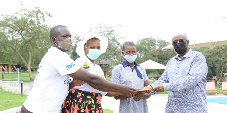 Brig Bakahumura hands over the envelope to Maximillah a student at Parental Care primary school Sanga in Kiruhura district. She is one of the beneficiaries of the annual school fees offer from Kigambira Safari Lodge, from the proceeds of the Kigambira Run attended by Champion Joshua Cheptegei on January 15 early this year. In the photo is Ali Seguya a Community assistant of Lake Mburo National Park and Ms Lynet, the mother of Maximillah.