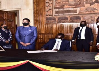 Ngoga signs in the condolence book as the Speaker and Deputy Speaker of Parliament of Uganda look on