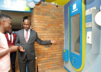 Honorable Henry Musasizi the State Minister of General Duties at the Ministry of Finance welcomes a customer to carry out a transaction during the launch of Post Bank's New Smart ATMs at their Forest mall branch in Lugogo