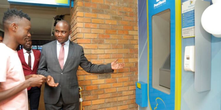 Honorable Henry Musasizi the State Minister of General Duties at the Ministry of Finance welcomes a customer to carry out a transaction during the launch of Post Bank's New Smart ATMs at their Forest mall branch in Lugogo