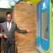 Honorable Henry Musasizi the State Minister of General Duties at the Ministry of Finance welcomes a customer to carry out a transaction during the launch of Post Bank's New Smart ATMs at their Forest mall branch in Lugogo