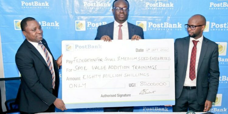 John Walugembe ED Federation of Small and Medium Enterprise (FSME) recieves a cheque from Julius Kakeeto the CEO Post Bank flanked by the Bank's ED Andrew Kabeera. The money is geared towards training and  empowering SME agri-businesses.