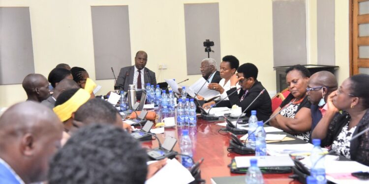 Ministers Tom Butime ( extreme far right with grey hair) and Peace Mutuuzo (in white) perusing through documents at the meeting with the committee