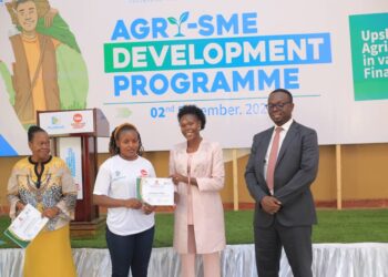 State Minister for Investment and Privatisation Hon. Evelyn Anite hands over a certificate to a participant in the Agro- SME development training at the closing ceremony as Post Bank Julius Kakeeto (right) looks on