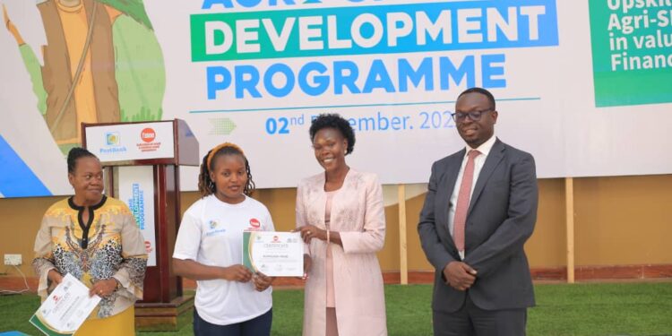State Minister for Investment and Privatisation Hon. Evelyn Anite hands over a certificate to a participant in the Agro- SME development training at the closing ceremony as Post Bank Julius Kakeeto (right) looks on