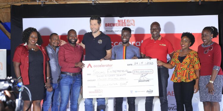 Nile Breweries Ltd MD Mr Adu Rando (4th Left) displays a dummy cheque after placing signature during the Accelerator Program launch event for Cohort 2023 at NBL Head Offices in Luzira.