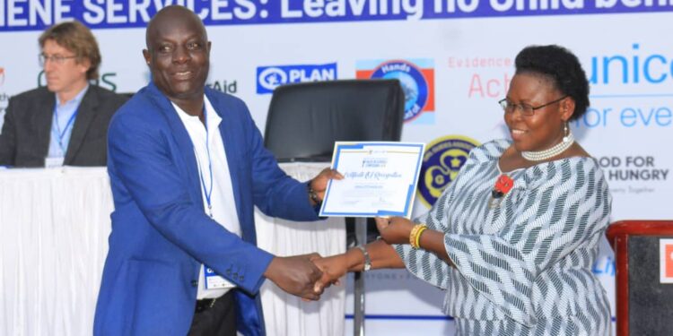 Hon. Joyce Moriku Kaduchu delivers a certificate of appreciation to Mr. Charles Opolot, the Executive Director for HAI Agency (U) Ltd, in appreciation of his efforts in leading the campaign on Wash in schools.