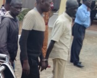 The accused wearing a black and cream sweater being escorted to Soroti grade one court where his case was mentioned today