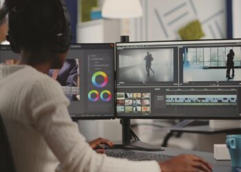 African video editor working with footage and sound, editing new project cutting film montage sitting in modern agency office. Woman using computer processing movie in post production software