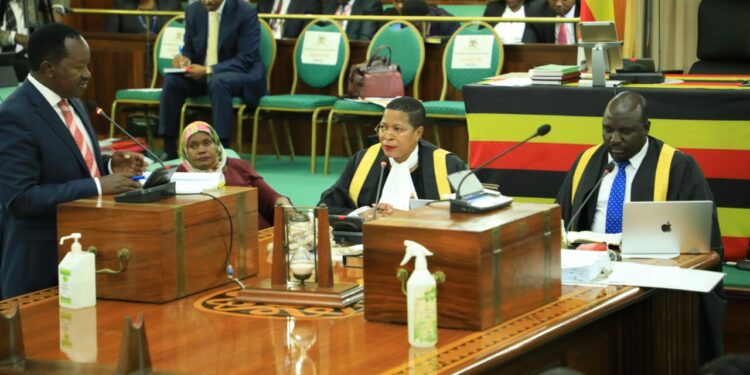 Hon. Wilson Kajwengye (L) speaking during the Committee of the Whole House on Tuesday 23 April 2024. Speaker, Anita Among (C) and a staff of Parliament (R) are at the Clerk’s Table